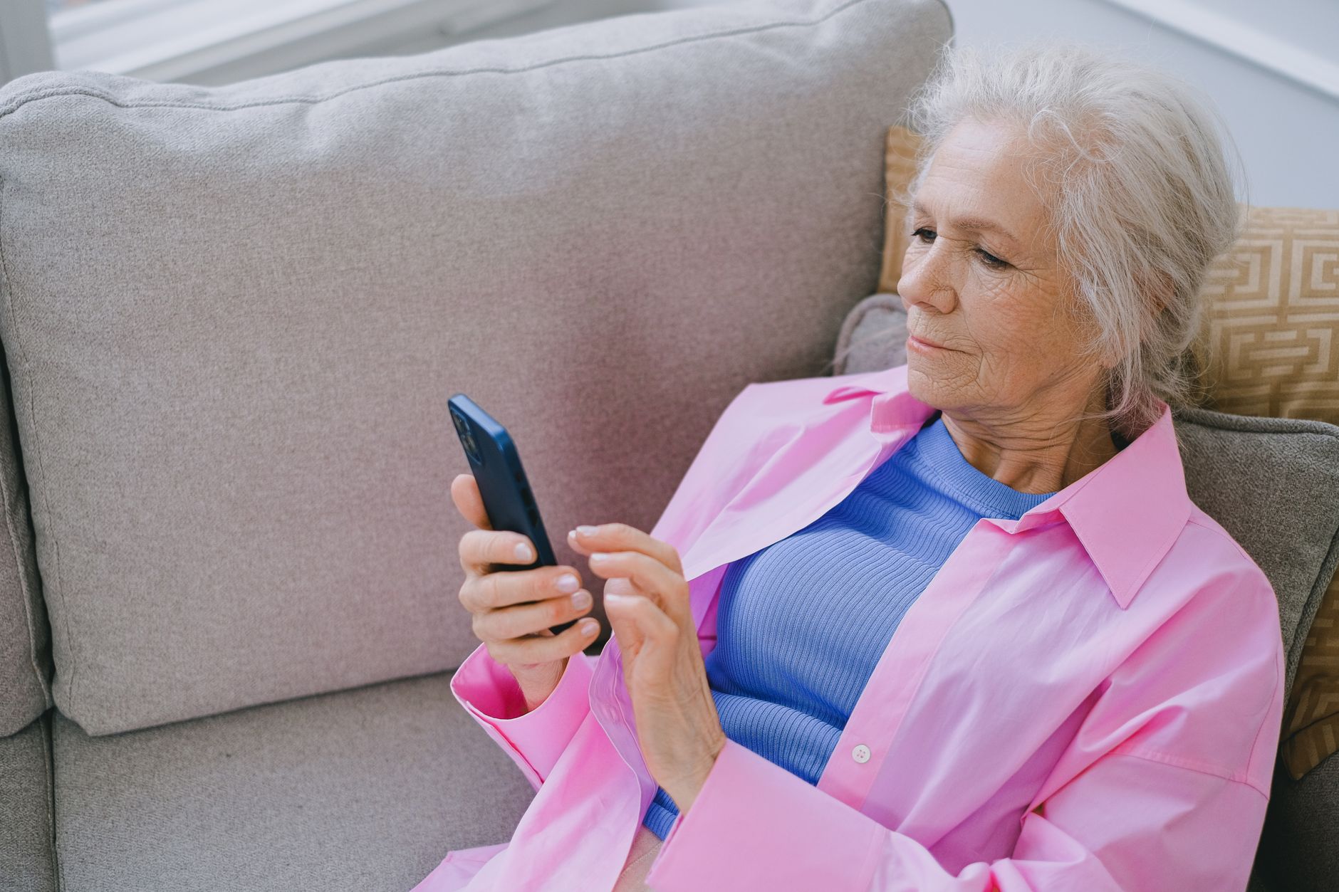 An older adult sits at a kitchen table holding a landline phone to one ear and looks worried, as if hearing a family emergency.