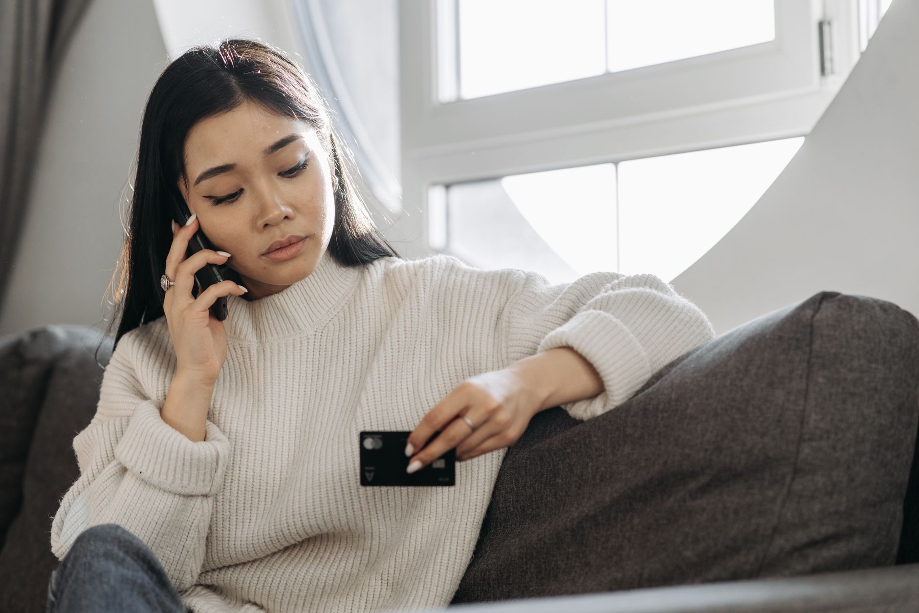 a woman talking on the phone while holding a credit card and looking concerned