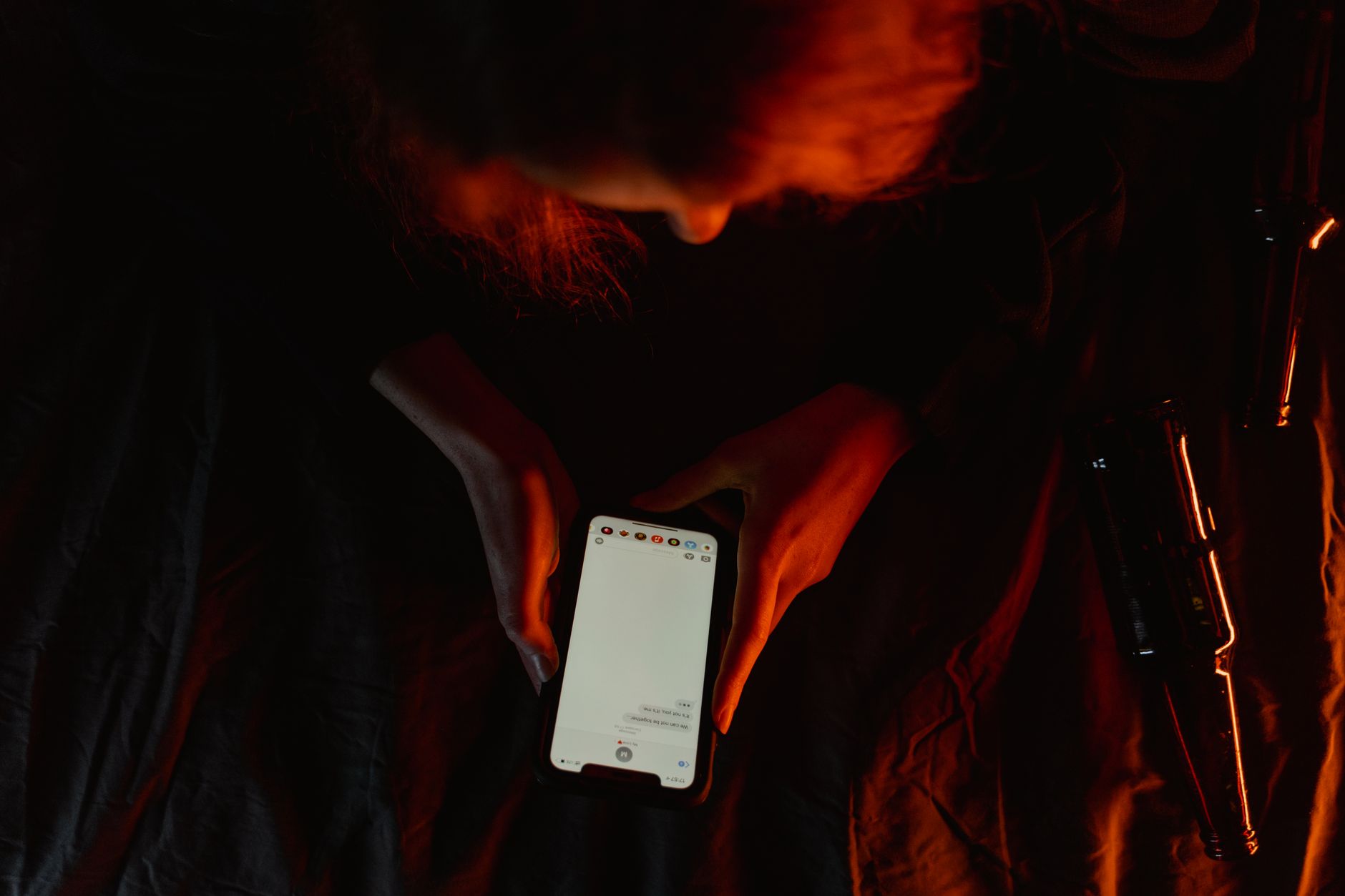 A person sits alone in a dark room, staring at a glowing smartphone screen with a worried expression